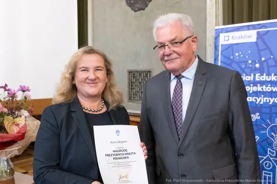 Wręczenie nagrody Prezydenta Miasta Krakowa. Uśmiechnięta kobieta z dyplomem i mężczyzna w okularach.