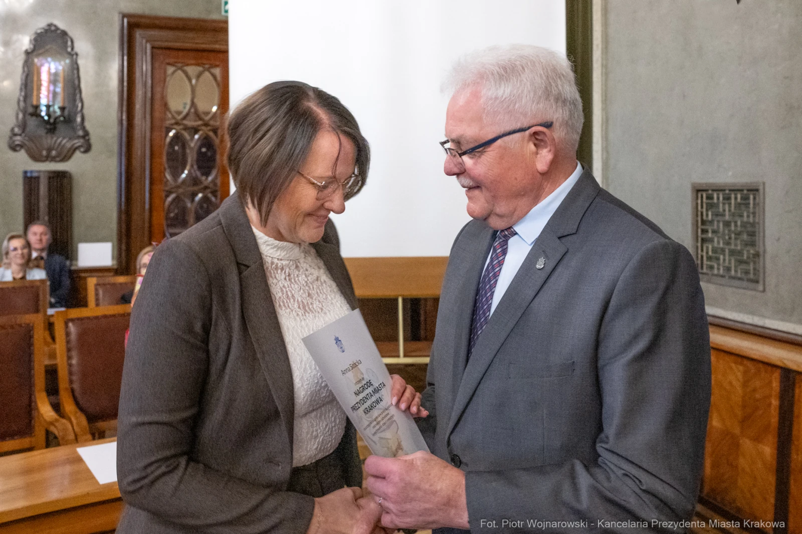 Wręczenie dokumentu w sali obrad, uśmiechnięte osoby w formalnych strojach.  Autor: Piotr Wojnarowski