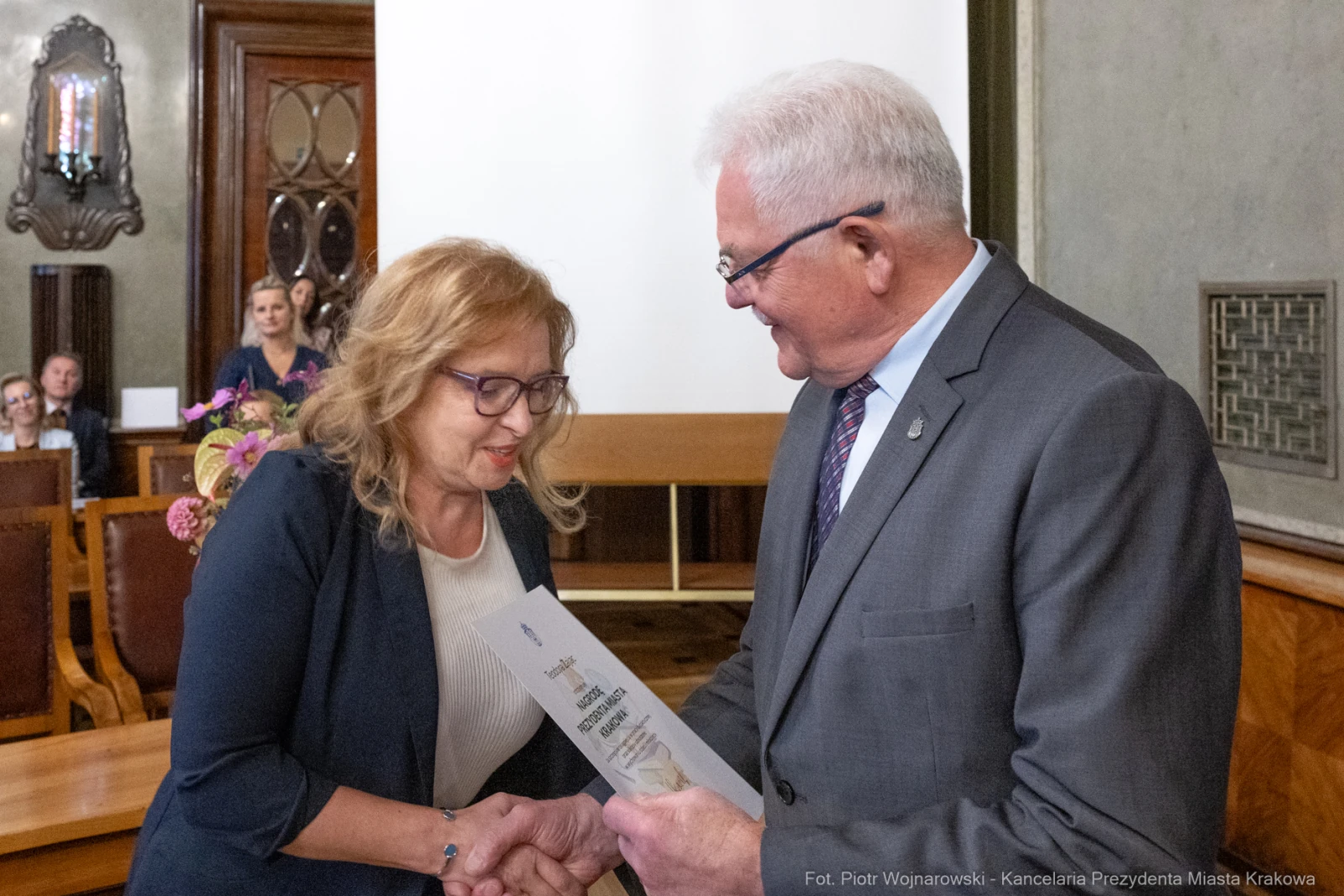 Wręczenie dyplomu przez mężczyznę kobiecie w sali z drewnianymi elementami.  Autor: Piotr Wojnarowski