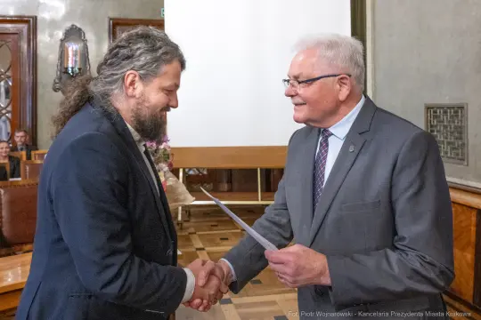 Mężczyźni uściskiem dłoni wymieniają dokumenty w formalnej atmosferze.