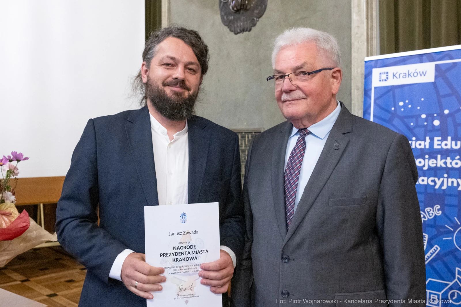 Mężczyzna z nagrodą w ręku stoi obok uśmiechniętego mężczyzny w garniturze.  Autor: Piotr Wojnarowski