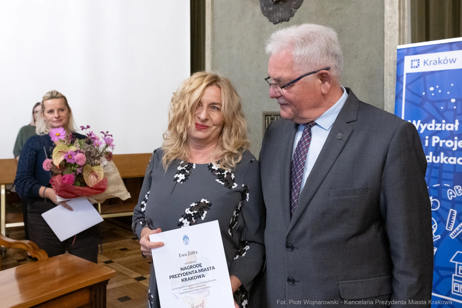 Kobieta z bukietem kwiatów i dyplomem, mężczyzna w garniturze obok niej.  Autor: Piotr Wojnarowski
