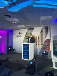 Mężczyzna przemawia przy podium z logo Cisco w nowoczesnym wnętrzu.
