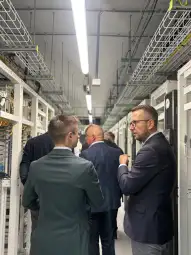 Dwóch mężczyzn rozmawia w serwerowni, w tle widoczne szafy z kablami.