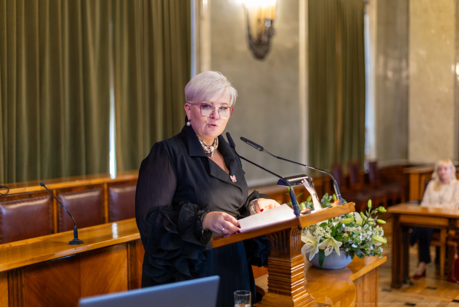 Kobieta w okularach wygłasza przemówienie przy mównicy w eleganckim wnętrzu.  Autor: Bogusław Świerzowski