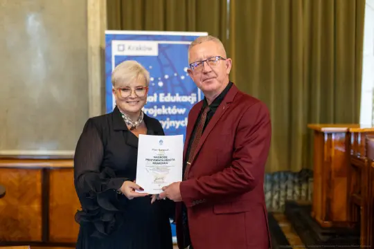 Wręczenie nagrody przez kobietę i mężczyznę, trzymających dyplom w sali konferencyjnej.