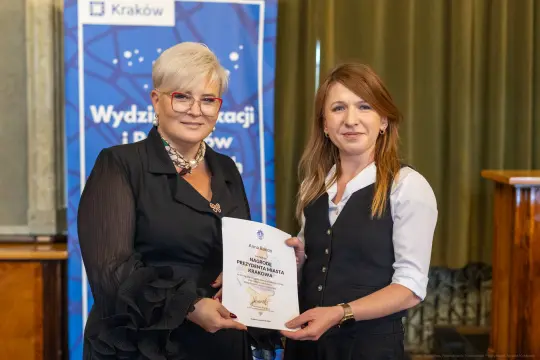 Dwie kobiety wręczają sobie dyplom w sali konferencyjnej.