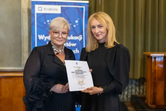 Kobiety wręczające dyplom w sali z dekoracjami.