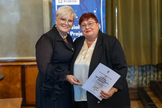 Dwie kobiety trzymają dyplom w eleganckim otoczeniu.