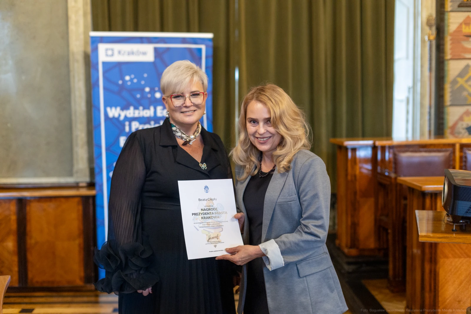 Dwie kobiety trzymające dyplom w sali z drewnianymi elementami.  Autor: Bogusław Świerzowski