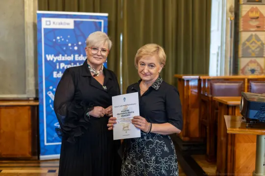 Dwie kobiety trzymają dokument w sali konferencyjnej.