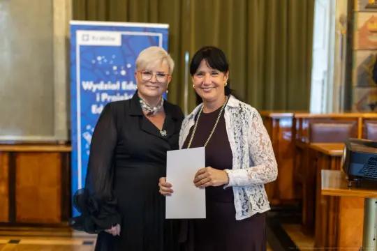 Dwie kobiety uśmiechają się, trzymając dokument w eleganckim otoczeniu.