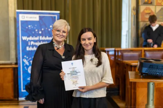 Kobieta wręczająca dyplom innej kobiecie w sali wykładowej.