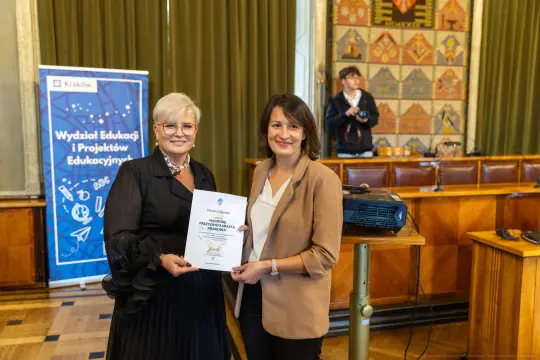 Wręczenie certyfikatu przez dwie kobiety w sali konferencyjnej.
