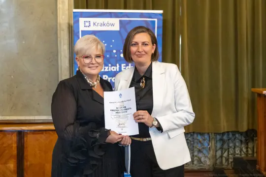Dwie kobiety trzymają dyplom w eleganckim otoczeniu.