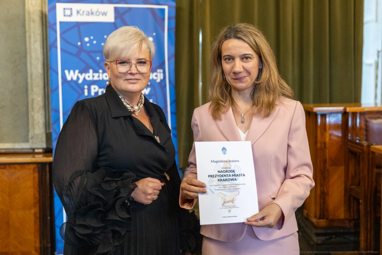 Dwie kobiety trzymają dokumenty, w tle baner z logo Krakowa.  Autor: Bogusław Świerzowski