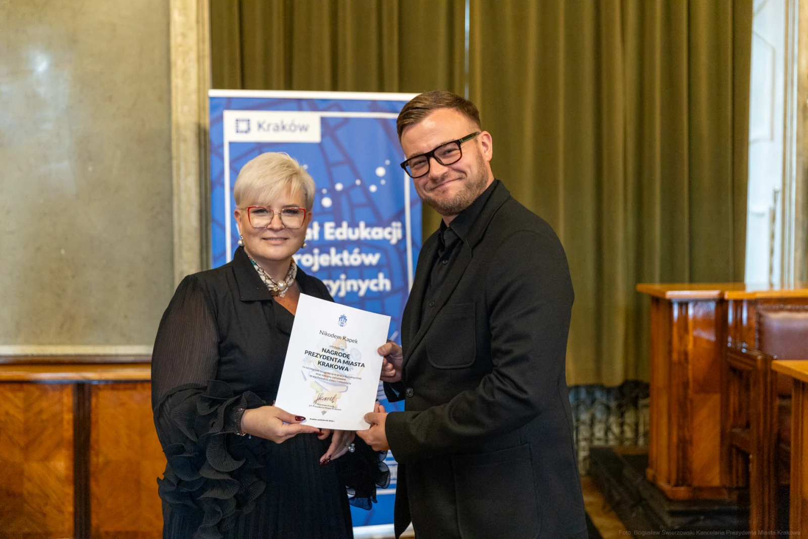 Osoba wręczająca dyplom drugiej osobie w eleganckim otoczeniu.  Autor: Bogusław Świerzowski