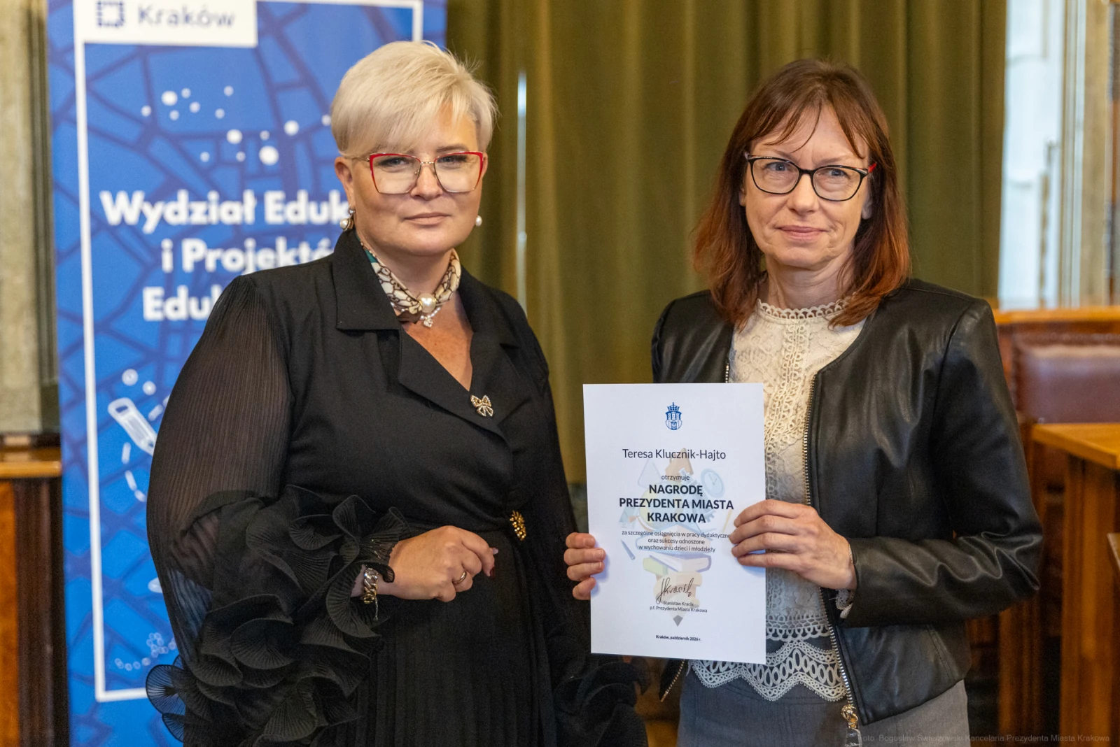 Dwie kobiety trzymają dyplom w sali z dekoracjami, jedna z nich w okularach.  Autor: Bogusław Świerzowski