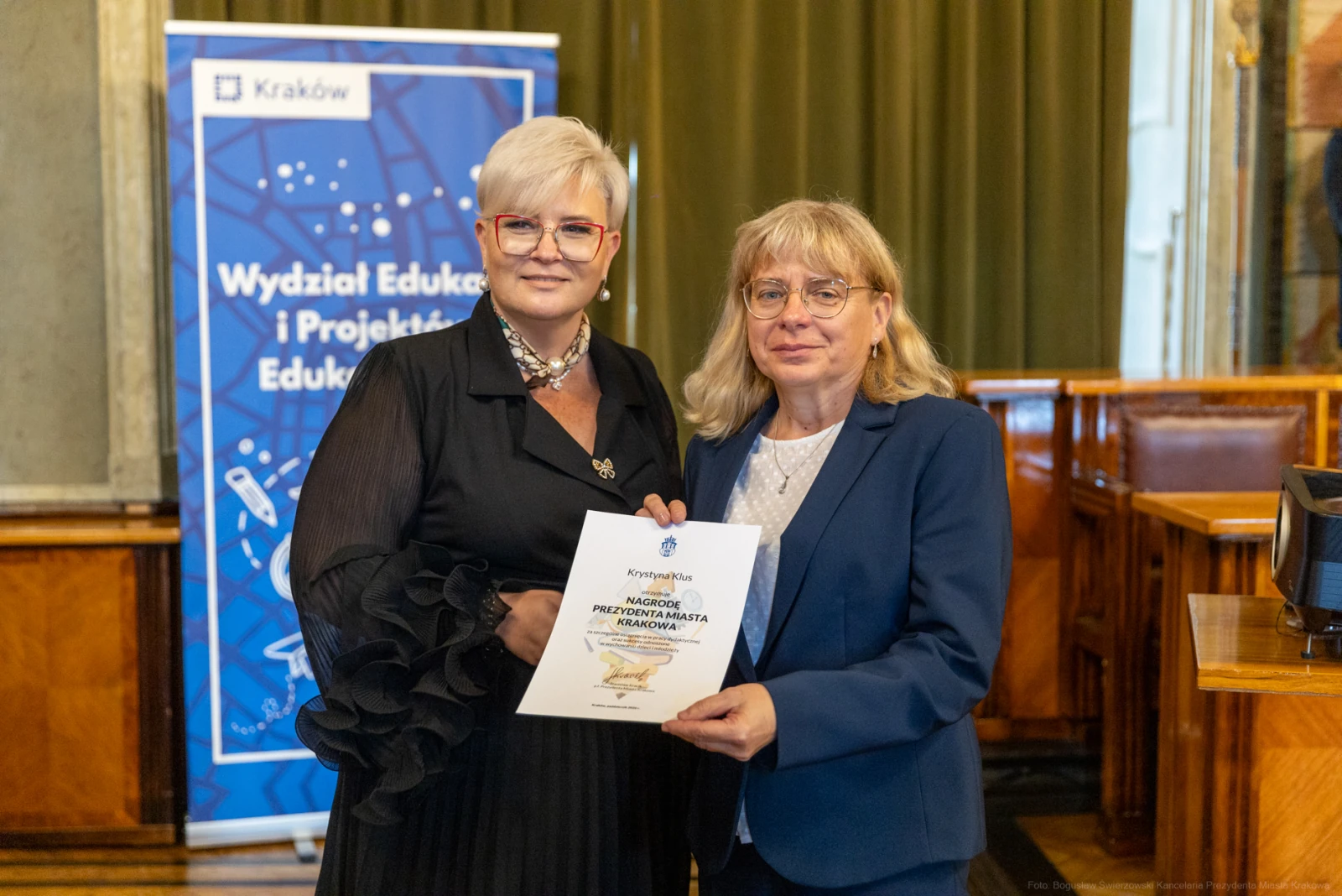 Dwie kobiety trzymają dyplom w sali z banerem Wydziału Edukacji i Projektów Edukacyjnych.  Autor: Bogusław Świerzowski