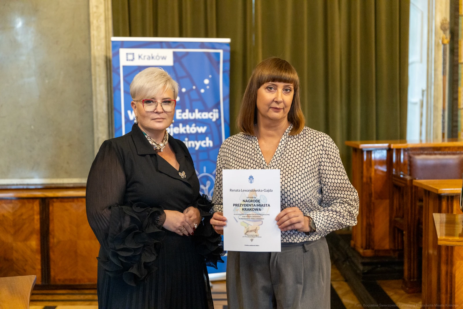Dwie kobiety trzymają dokument w sali, w tle baner dotyczący edukacji.  Autor: Bogusław Świerzowski