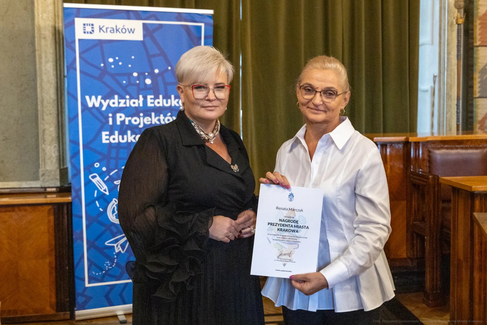 Dwie kobiety trzymają dyplom w sali z dekoracjami i plakatem Wydziału Edukacji.  Autor: Bogusław Świerzowski