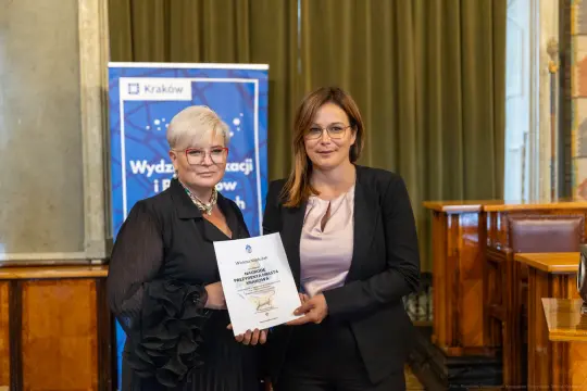 Dwie kobiety trzymają dokument w sali konferencyjnej.