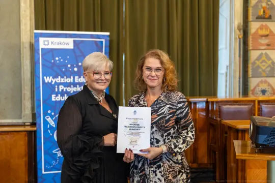Dwie kobiety trzymające dokument w sali konferencyjnej.