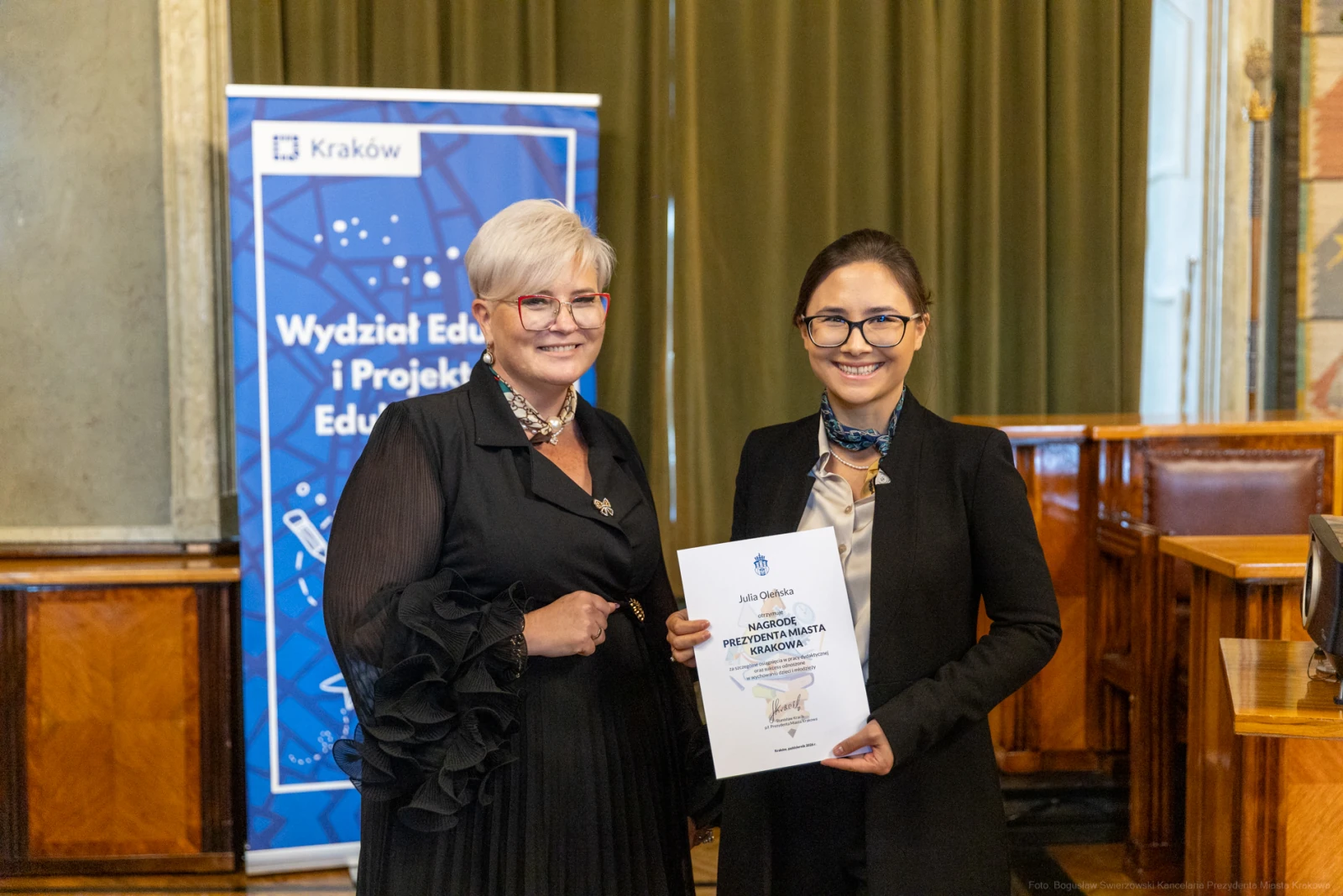 Dwie kobiety trzymają dokument w sali konferencyjnej. W tle baner Wydziału Edukacji i Projektów Edukacyjnych.  Autor: Bogusław Świerzowski