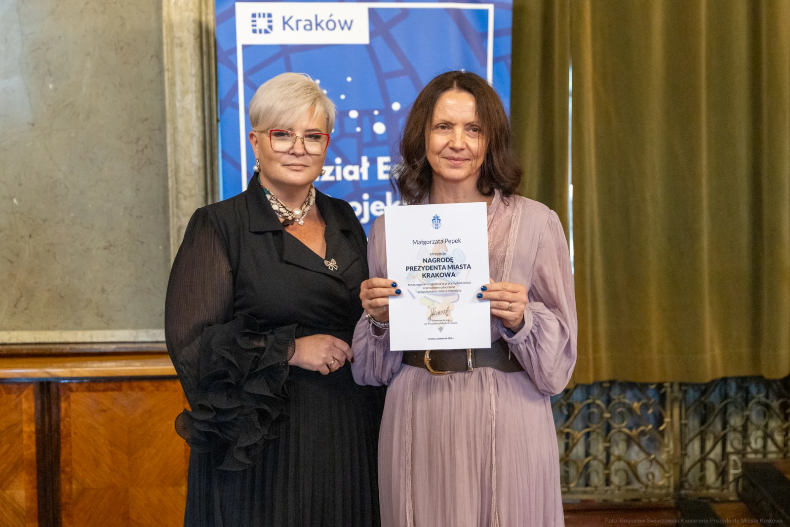 Dwie kobiety trzymające dyplom w eleganckim wnętrzu.  Autor: Bogusław Świerzowski