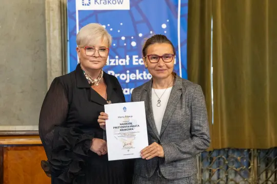 Dwie kobiety trzymające dyplom w eleganckim otoczeniu.