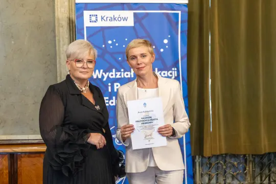 Dwie kobiety trzymają certyfikat w sali z dekoracjami.