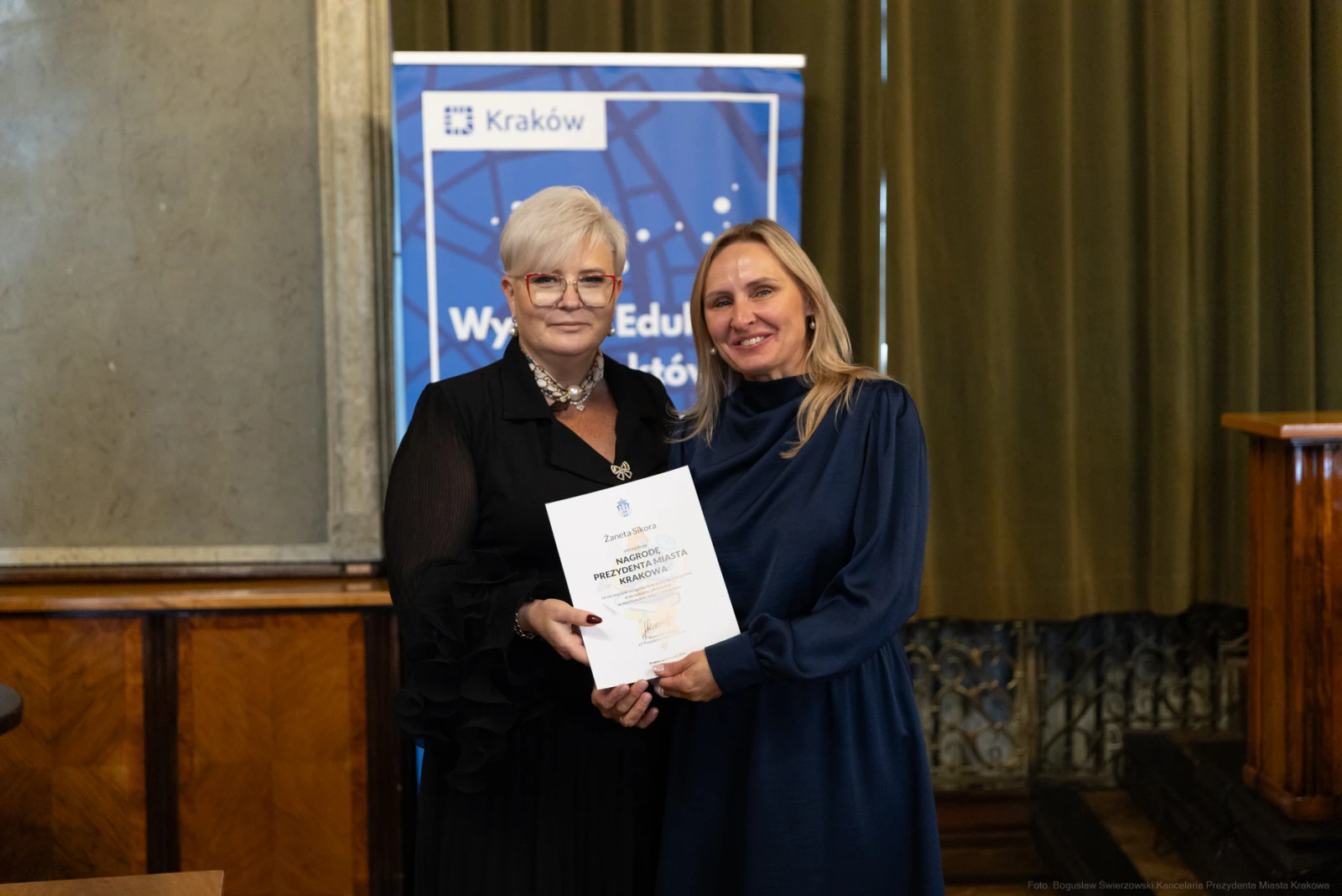 Dwie kobiety trzymające dyplom w sali z dekoracjami.  Autor: Bogusław Świerzowski
