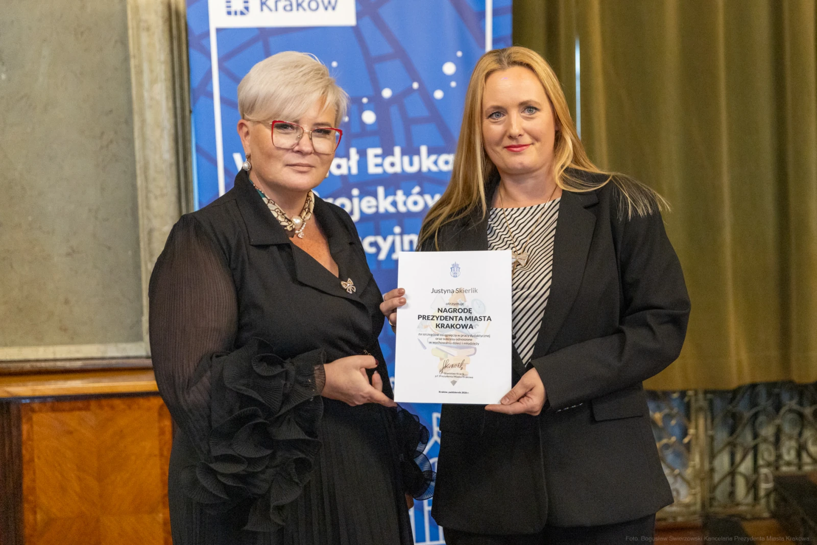Dwie kobiety wręczają sobie dyplom w sali z dekoracjami.  Autor: Bogusław Świerzowski