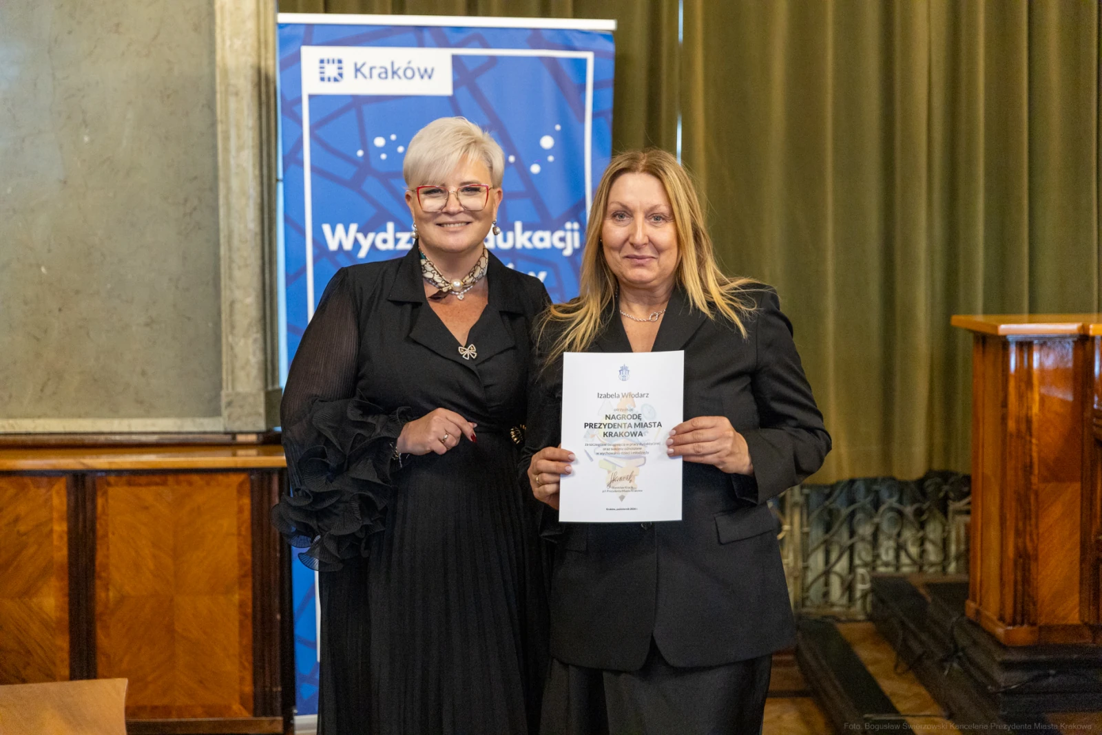 Dwie kobiety trzymają dyplom w sali z zielonymi zasłonami i banerem Wydziału Edukacji.  Autor: Bogusław Świerzowski