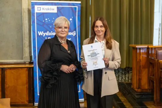 Dwie kobiety trzymające dyplom w sali z zielonymi zasłonami.