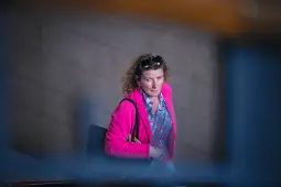 Kobieta w różowej marynarce z okularami na głowie, idąca po schodach.