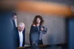 Kobieta z kręconymi włosami w czarnej sukience idzie schodami, obok niej mężczyzna w jasnej koszuli.