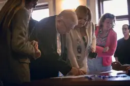 Grupa osób uczestniczy w dyskusji przy stole, jedna osoba pisze na kartce.