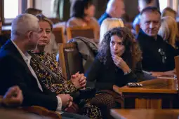 Grupa ludzi w sali, rozmawiających i słuchających.
