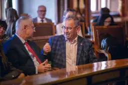 Dwaj mężczyźni rozmawiają w sali obrad, w tle inni uczestnicy spotkania.