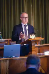 Mężczyzna w garniturze przemawia z mównicy podczas konferencji.