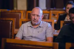 Mężczyzna w jasnej koszuli siedzi w sali z drewnianymi ławami.