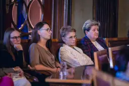 Grupa kobiet siedzących w sali, skupionych na wydarzeniu.