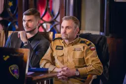 Dwaj mężczyźni siedzący przy stole, jeden w mundurze, drugi w eleganckim ubraniu.