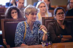 Kobieta z mikrofonem zadaje pytanie podczas konferencji, w tle uczestnicy.