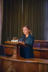 Kobieta przemawia z mównicy w sali obrad.