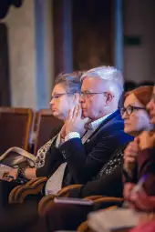 Grupa osób siedzących na wykładzie, skupionych na prelekcji.