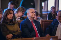 Grupa osób siedzących w sali, jedna z nich w garniturze z czerwonym krawatem.