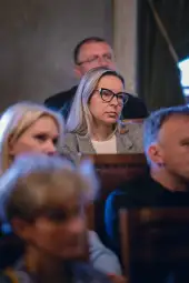 Kobieta w okularach, skupiona na wykładzie, w tle inni uczestnicy.