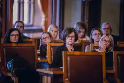 Grupa osób siedzących na sali, skupionych na prezentacji lub dyskusji.
